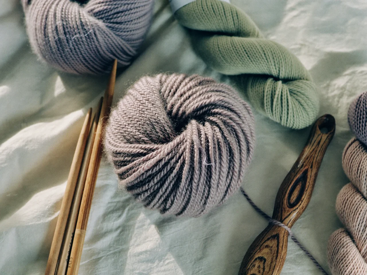 Illustrative overhead view of soft wool skeins, bamboo knitting needles and a crochet hook on linen