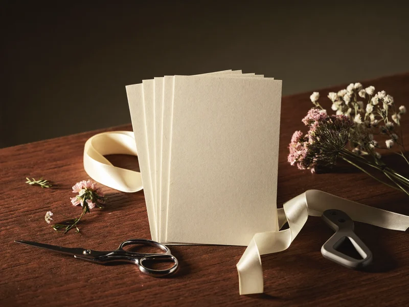 Illustrative blank cream cards with pressed flowers, ribbon, scissors and a paper trimmer