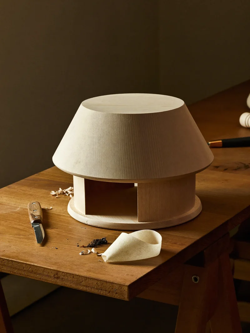 Illustrative partly assembled wooden birdhouse with whittling knife, sandpaper and wood shavings